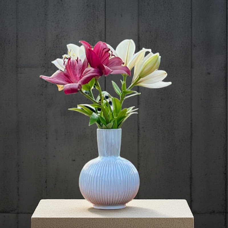 weiße, bauchige Keramikvase mit Lilien bestückt